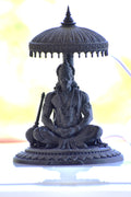 Statue of a seated figure with an umbrella-like structure on a white background