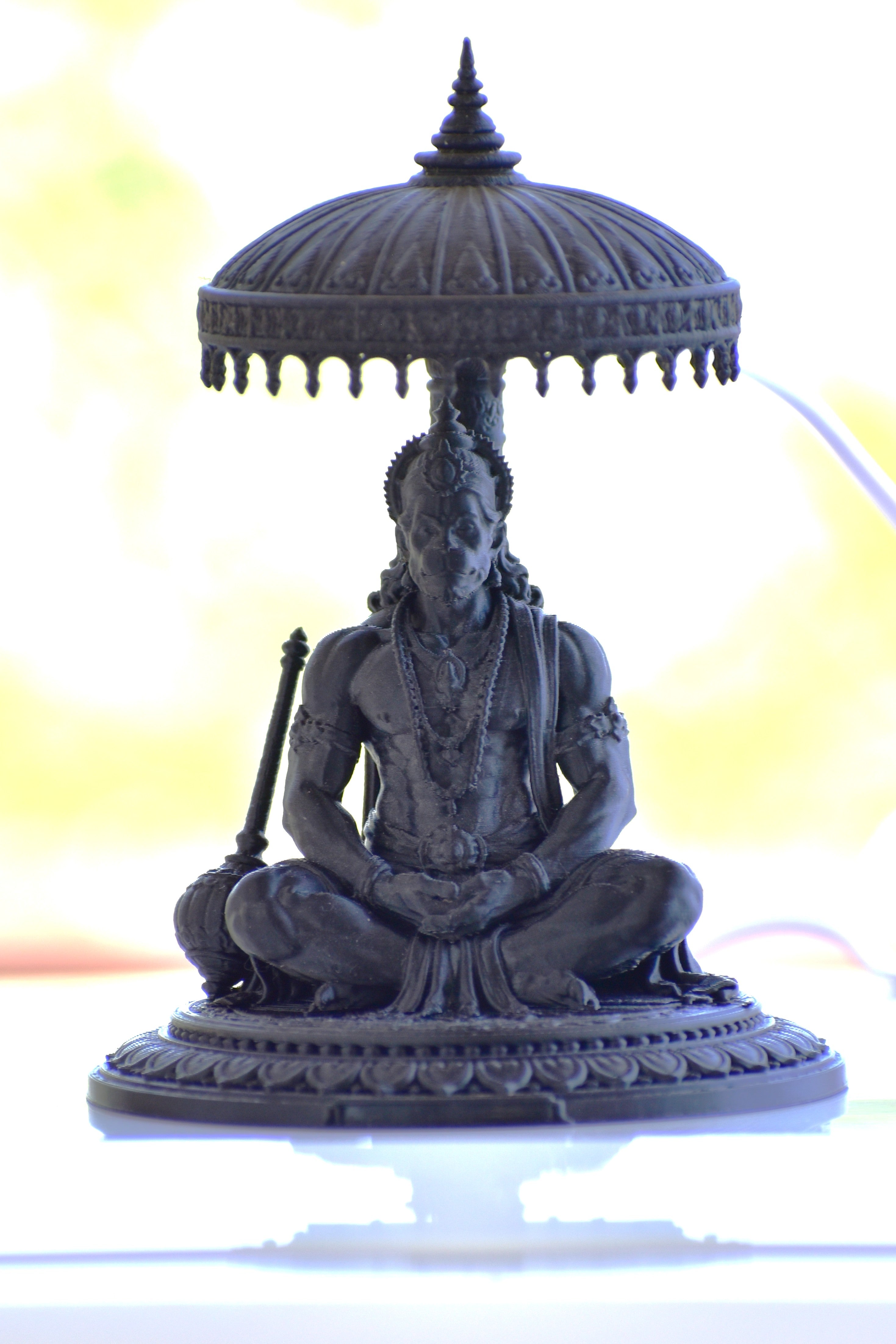 Statue of a seated figure with an umbrella-like structure on a white background