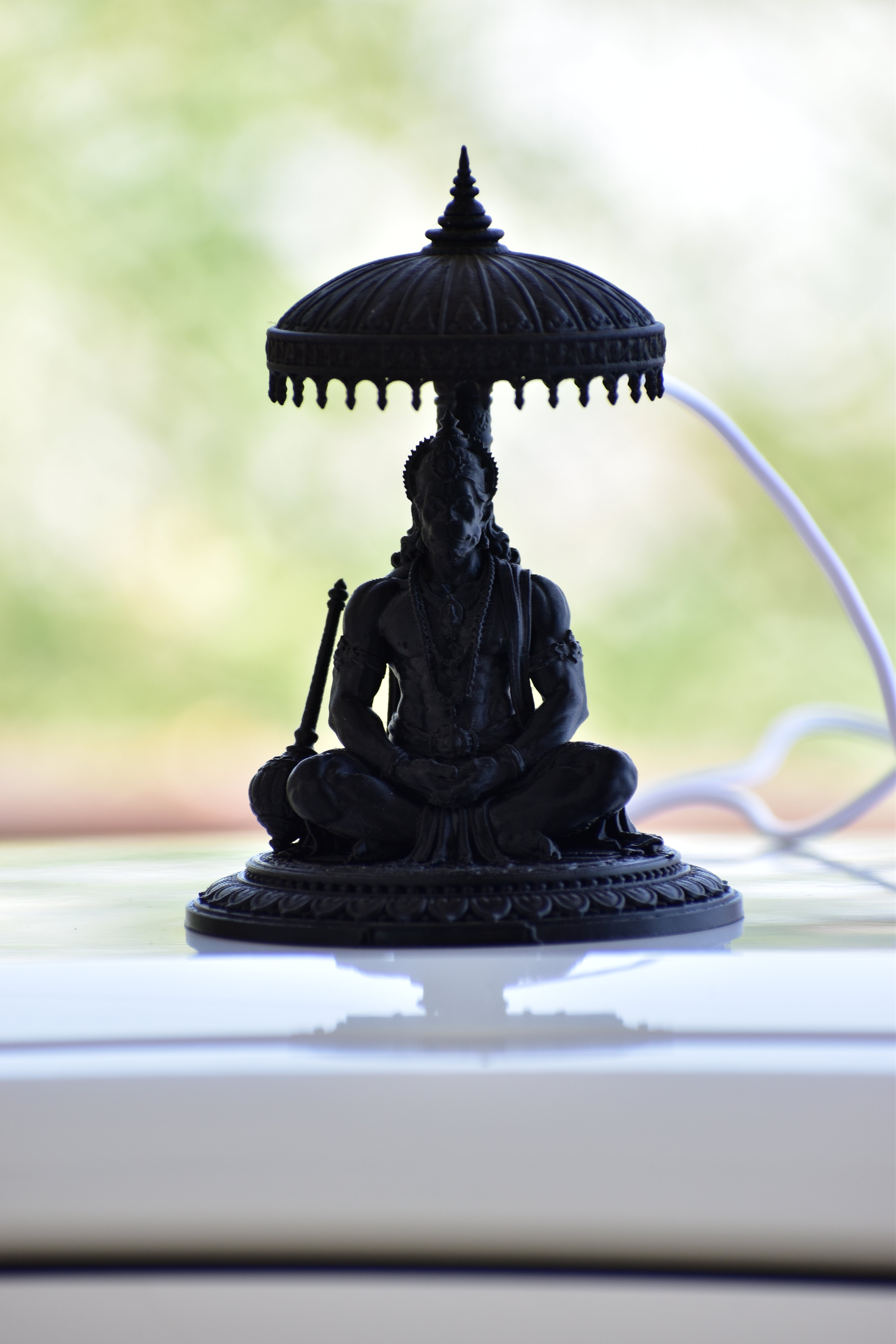 Black statue of a seated figure under an umbrella on a reflective surface with a blurred natural background